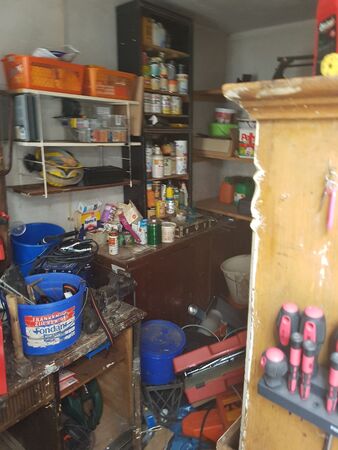 Unordentliche Werkstatt mit Werkzeugen, Farbdosen, Regalen und Aufbewahrungsboxen.