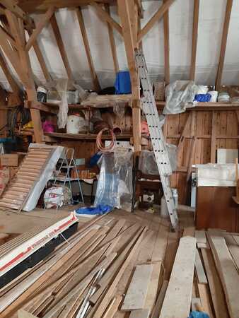 Dachboden mit Holzlatten, Baumaterial, Werkzeugen und Leiter für Renovierungsarbeiten.