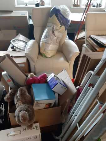 Ein weißer Sessel steht inmitten vieler Umzugskartons und Haushaltsgegenstände im Raum.